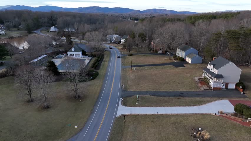 Driving cars on rural intersection during winter season in USA. Single family houses with front yard in Virginia. House with frozen swimming pool at sunrise. Aerial forward wide shot.