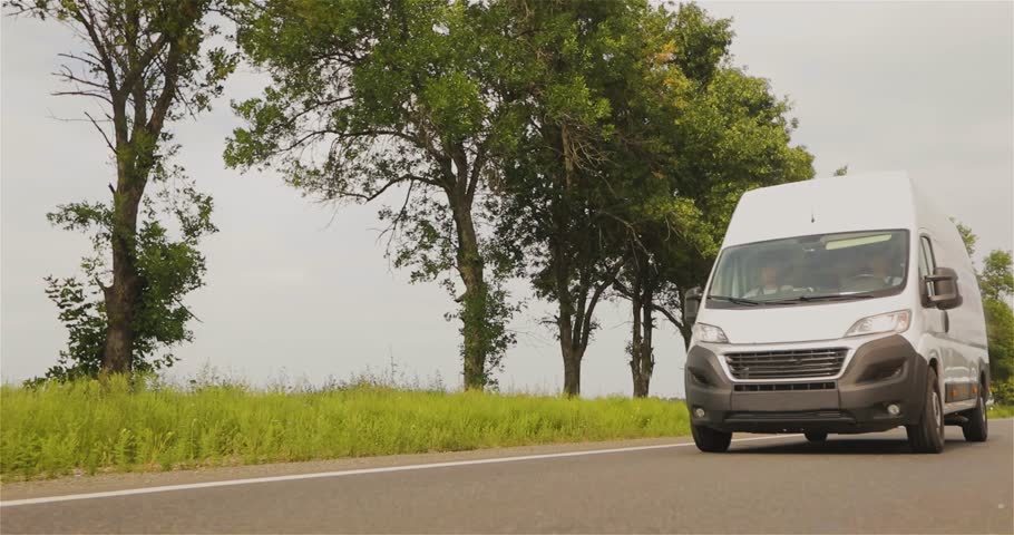 A white delivery or service van is driving down the road. White cargo minibus on the highway. Cargo minibus drives on the highway in sunny weather.