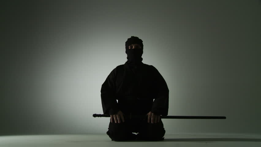 Low angle view of a masked ninja unsheathing a short sword, holding it and then