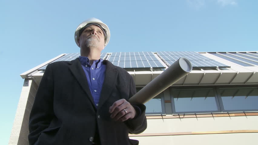 Architect stands proudly with a tube of blue prints in front of solar panels