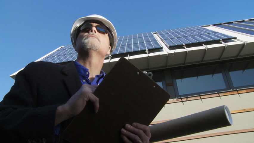 Architect makes notes in front a newly installed solar array on a roof. Could