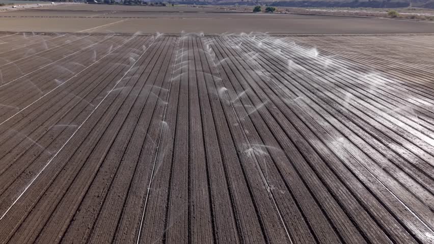 Irrigation System Spraying Water On A Open Dirt Agricultural Field In California, Aerial Flyover.