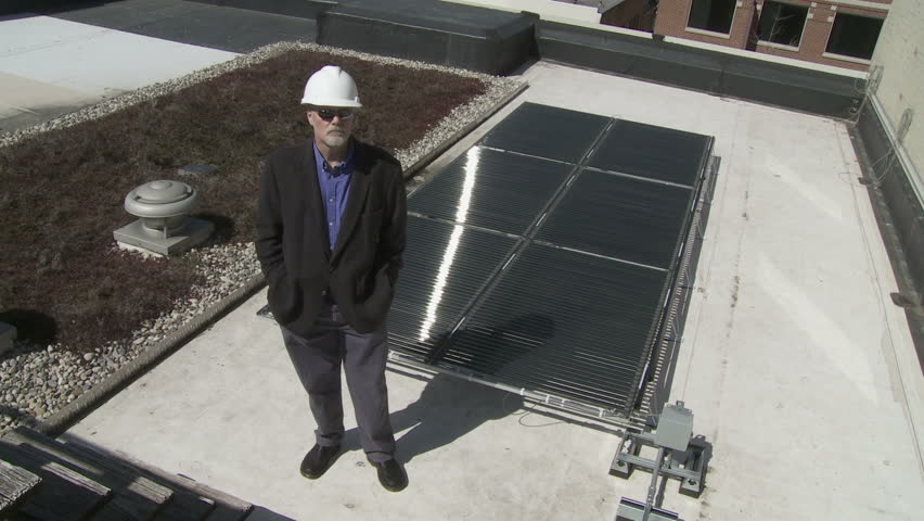 Technician stands in front of a solar power installation on a roof top. This