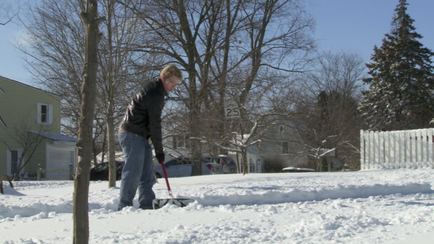 Teenager shoveling snow from a drive in the USA. Hand held wide shot.