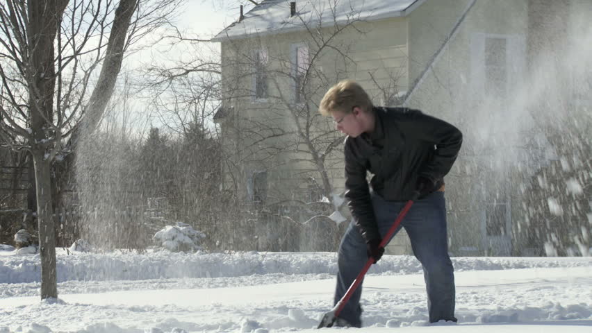 Teenager shovels snow quickly in the Mid West, USA. Full length shot from side