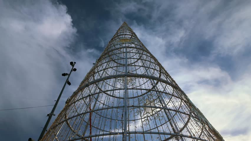Low-angle view of a massive Christmas tree structure in Valletta, Malta. The metal frame is decorated with festive lights and stars, set against a dramatic sky, creating a stunning holiday atmosphere.