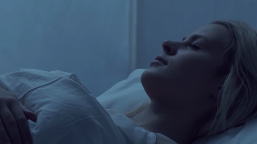 Young woman lying in the bed at night and having insomnia disease. Beautiful blond sleeping girl. Twilight in the bedroom, moonlight from the window. Sleeplessness, health and rest concept.