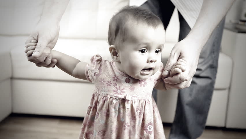 Smiling baby with father helping baby with first steps inside 