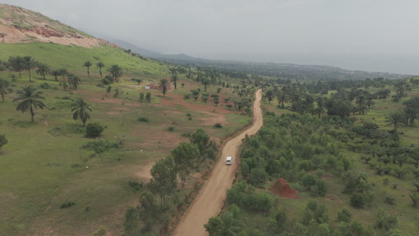 Following drone shot of a white bus or van driving on a rocky road near the town of Kimina Bujumbura Burundi Africa on a warm day with the landscape in the back LOG