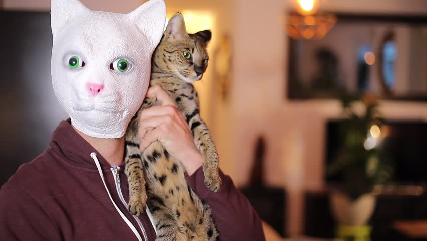Man wearing a cut rubber mask holding a real cat 