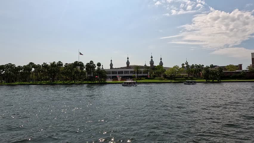 footage of boats sailing along the Hillsborough River with lush green trees along the banks at the Tampa Riverwalk in Tampa Florida USA