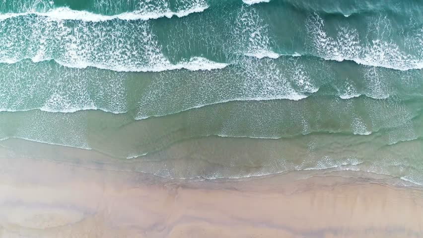 Aerial view of the beach with gentle waves washing upon the shore, creating a serene scene.