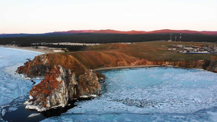 Flight over the rocky Cape Burkhan to the shore of Olkhon Island. Lake Baikal spring day at sunset. Time of ice melting on the lake, ice drift.
