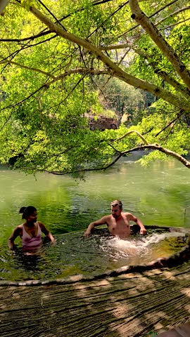 Two individuals enjoy a tranquil moment in a natural hot spring, embracing the serene atmosphere and soothing water. a couple in a hot tub by the river in Thailand