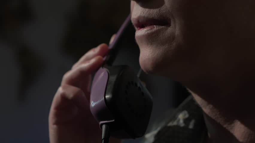 Woman communicates calmly speaking on landline phone in dimly lit indoors in evening