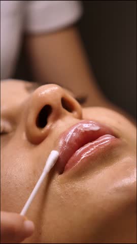 Moisturizing and nourishing lips in a beauty salon for a young Caucasian woman, close-up, vertical, stories