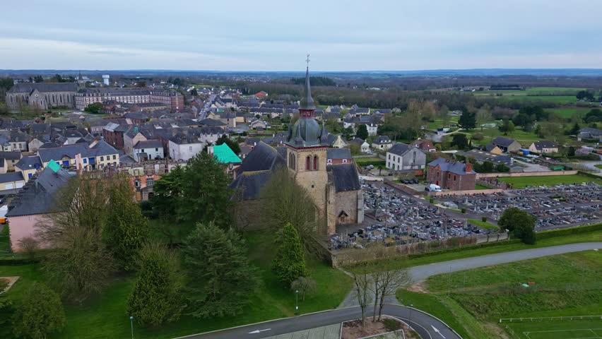 Panning drone movement near the Abbey of Saint-Méen-le-Grand monastery with parking area and cityscape, St. Méen-le-Grand, Ille-et -Vilaine, Bretagne in France.