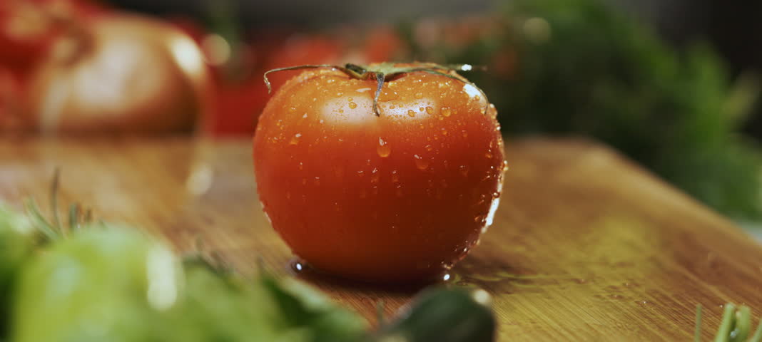 A professional male chef aggressively cutting a red tomato in slow-motion