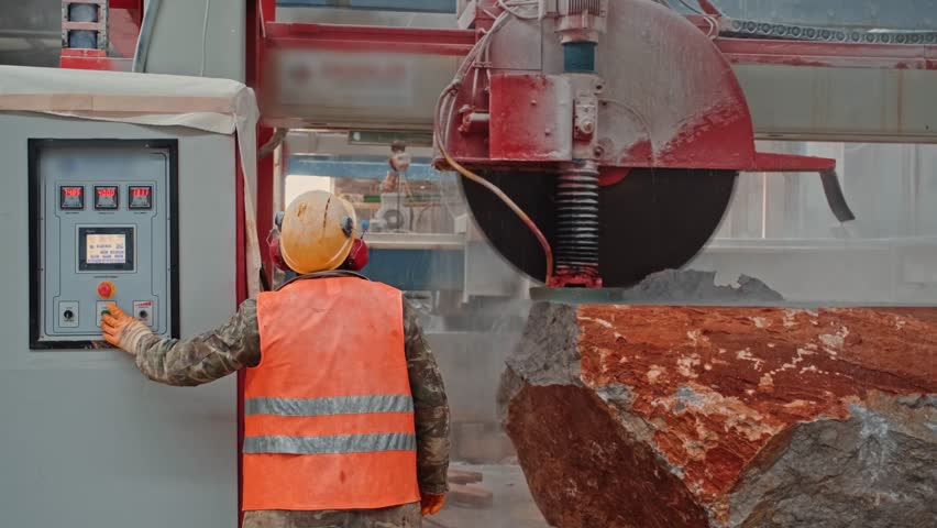 Activating an industrial stone-cutting machine. The operator starts an automated cutting system to slice large marble blocks.