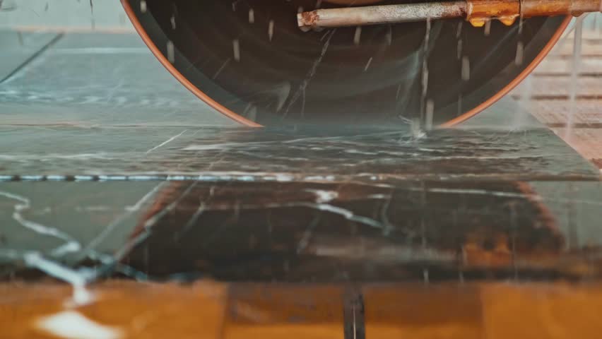 Marble slab cutting and water cooling process. Industrial machines precisely cut stone slabs while spraying water to cool the blades.