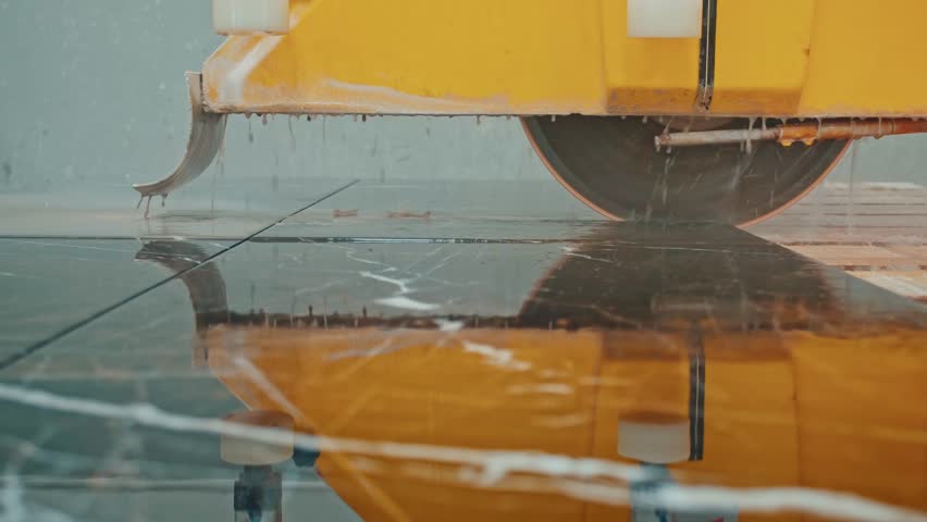 Marble slab cutting and water cooling process. Industrial machines precisely cut stone slabs while spraying water to cool the blades.