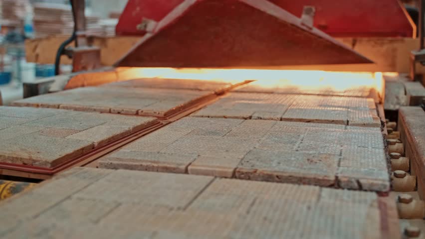 Ceramic tile production line during the firing process. High-temperature industrial kiln hardens the ceramic surfaces.
