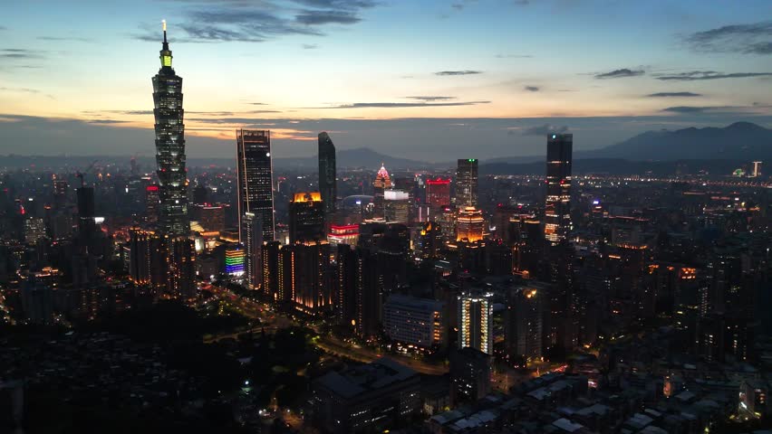 Aerial view at night above Downtown Taipei, the vibrant capital of Taiwan, with 101 Tower standing out amid skyscrapers in XinYi Commercial District and city lights dazzling under moody twilight sky