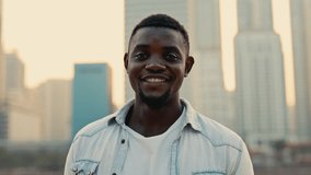 Portrait of calm African American man wearing denim jacket standing against cityscape. Handsome guy stands alone looking at camera on large city street. Male model in dusk megapolis - Powered by Shutterstock - Get 15% off with code: PIKWIZARD15