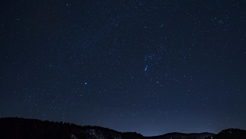 Timelapse of a clear night sky with moving stars and constellations above snow capped peaks, highlighting Earth