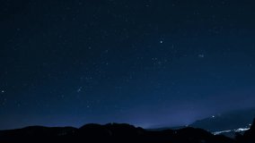 Timelapse showing stars moving across a clear night sky, with mountain silhouettes in the foreground and faint city lights at the base. - Powered by Shutterstock - Get 15% off with code: PIKWIZARD15