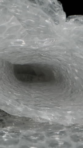 Vertical video. Dolly slider close-up moving inside a tunnel of bubble wrap, creating a textured and translucent effect with a soft-focus depth, highlighting the intricate pattern of protective air bu