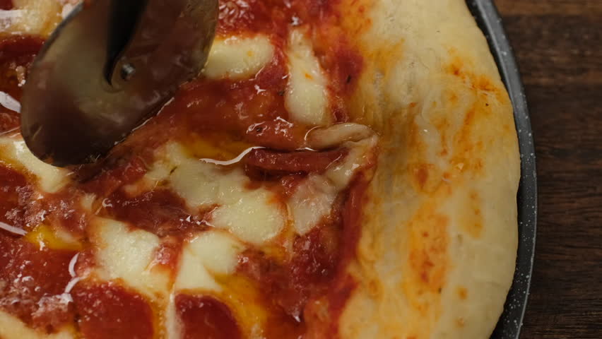 Hand cutting pizza. Pizza slicing into pieces with knife, close up