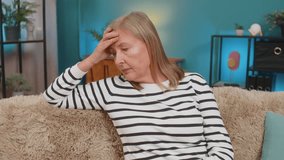 Caucasian mature woman places hand on forehead, sitting on sofa at home, showing frustration helplessness. Grandmother expresses stress disappointment after bad day, feeling overwhelmed disheartened - Powered by Shutterstock - Get 15% off with code: PIKWIZARD15