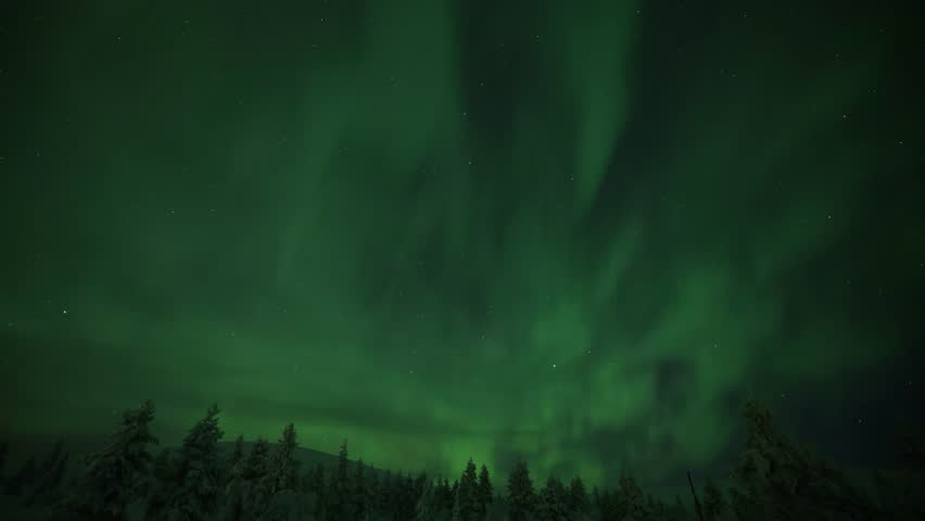 Green and red aurora borealis crossing the starry night sky over snowy mountains and forest in lapland finland and sweden. 4K resolution footage time lapse.