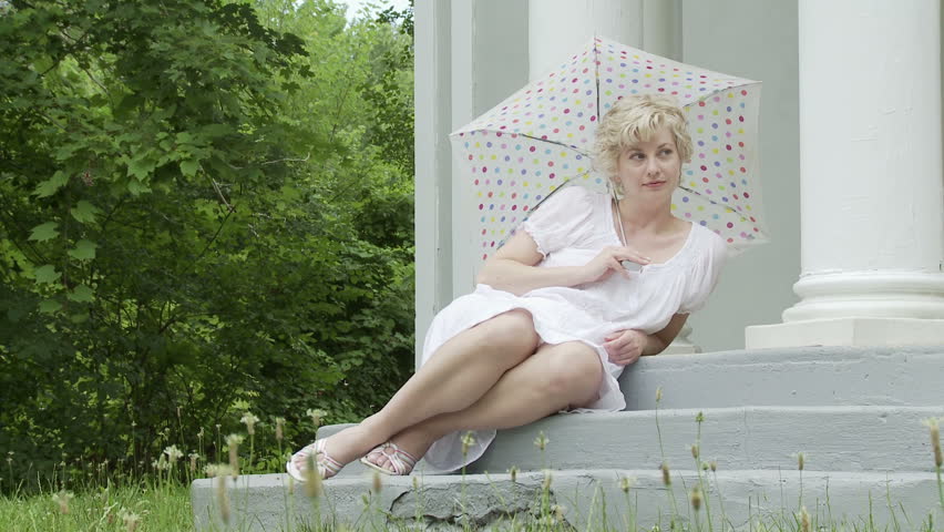 Girl with a polka dot parasol reclines on the steps of an outdoor gazebo. Dolly