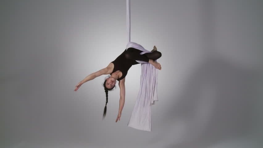 Aerial yoga practitioner stretches herself while suspended on silk. Wide shot on