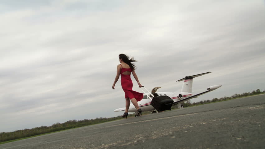 Attractive girl in a red dress walks with her suitcase across a runway in front