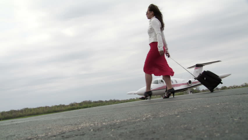 Attractive girl wearing a red dress and white jacket, walks with her suitcase
