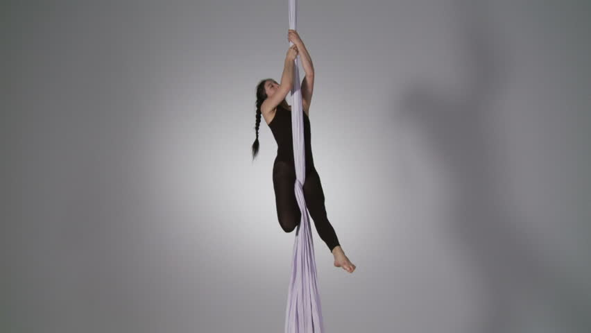 Aerial yoga practitioner holds herself in position on silk supports. Wide shot