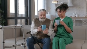 Positive charming black female nurse in uniform and attractive grey haired senior man on retirement enjoying leisure, friendly chatting and sharing while drinking coffee from mugs in care home. - Powered by Shutterstock - Get 15% off with code: PIKWIZARD15
