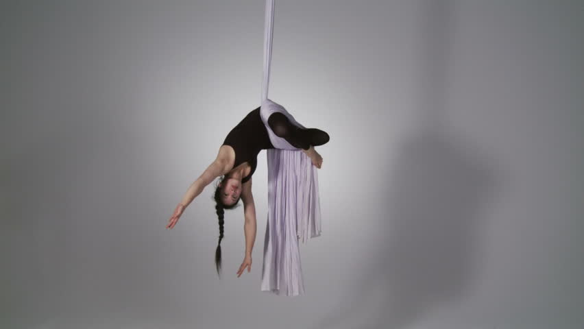 Aerial yoga practitioner stretches herself while suspended on silk. Wide shot on