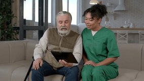 Cheerful senior grey haired man and positive African American female caregiver in uniform networking , browsing and discussing social media content online on digital tablet in nursing home. - Powered by Shutterstock - Get 15% off with code: PIKWIZARD15