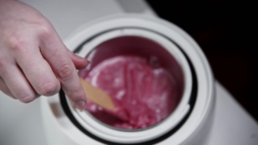 Depilation master melts pink wax in the heater and mixing it using a spatula