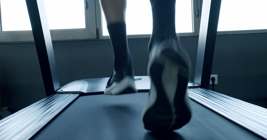 A dynamic, low angle shot of a person's legs running on a modern treadmill. Focus on determination and fitness in a well-lit gym environment. Close-Up View of a Person Running on a Treadmill in a Gym