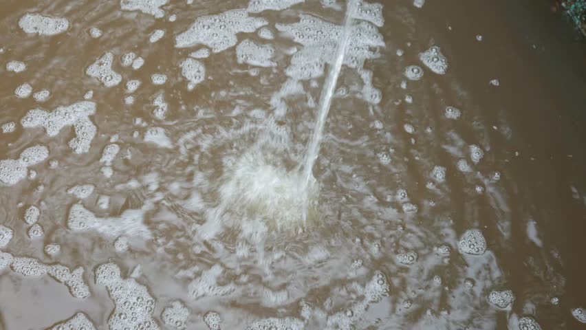 Ripples in a puddled pond as faucet water drips into it.