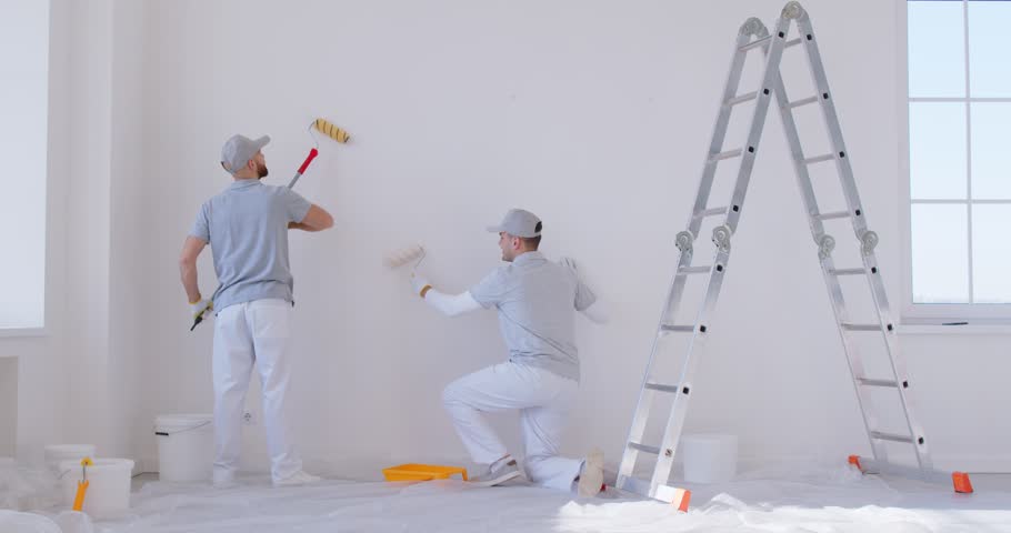 Professional team of man decorators paint walls with paint rollers, doing repair renovation of apartment, trying to finish their task in time. House decoration and improvement concept