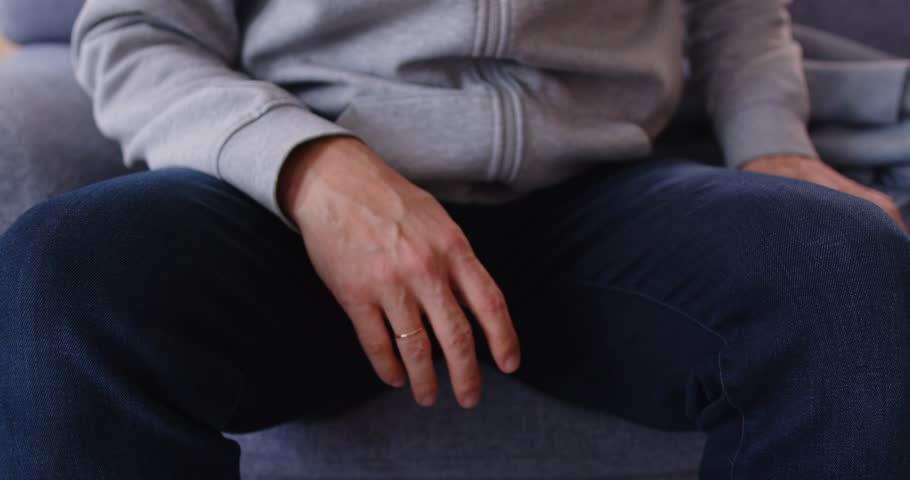 Close up cropped view of poor upset man sitting on sofa and opening wallet with small amount of coins. Displeased person with no money having financial problems, lacking budget, bankruptcy or debts.