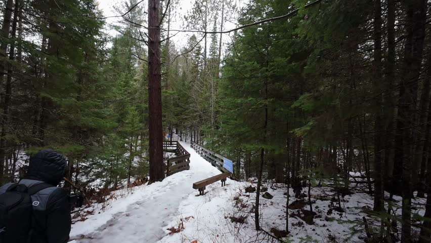 A man hikes across a snow-covered bridge on an overcast winter day in Algonquin Park, Ontario, Canada
