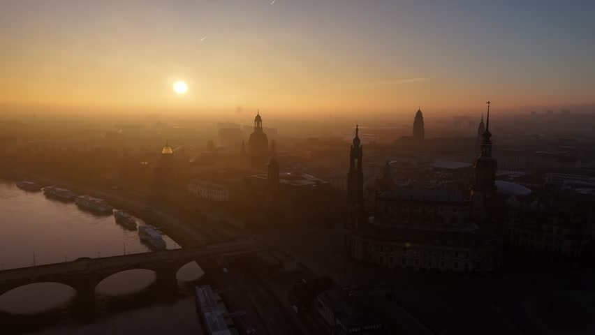 A drone view of silhouetted skyline of Dresden city with churches, river and bridge at sunset time in Germany