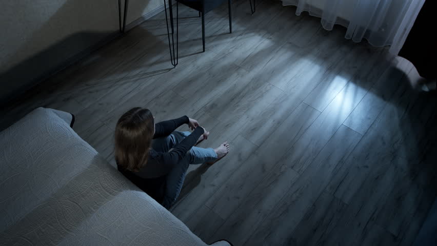 Lonely woman sitting on the floor in a dark room. Concept of problems, depression and stress. Mental health. Domestic violence.